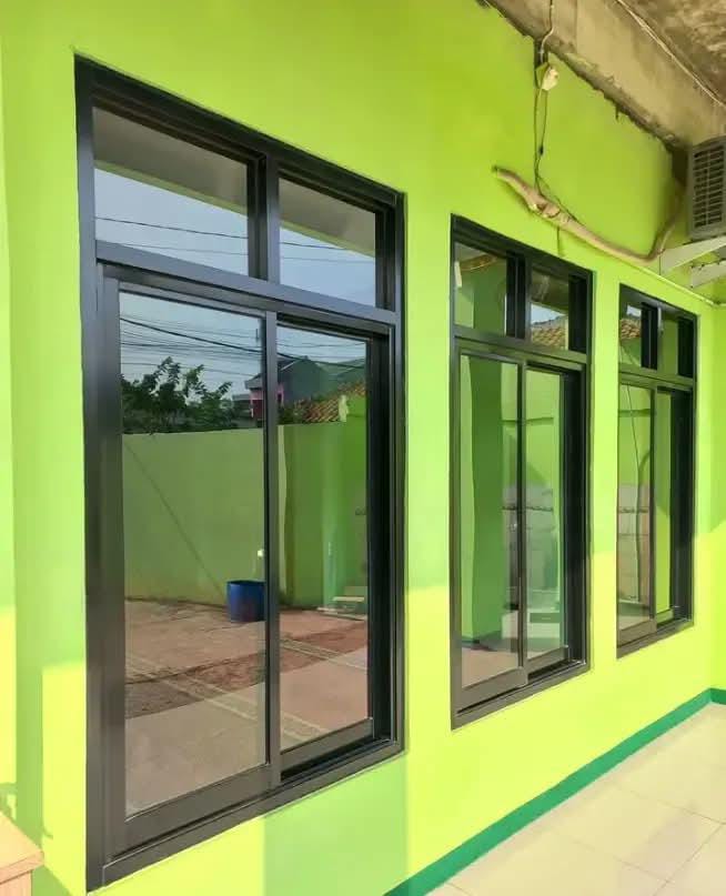 Tiga jendela sliding aluminium hitam terpasang di dinding hijau oleh Toko Lor Aluminium